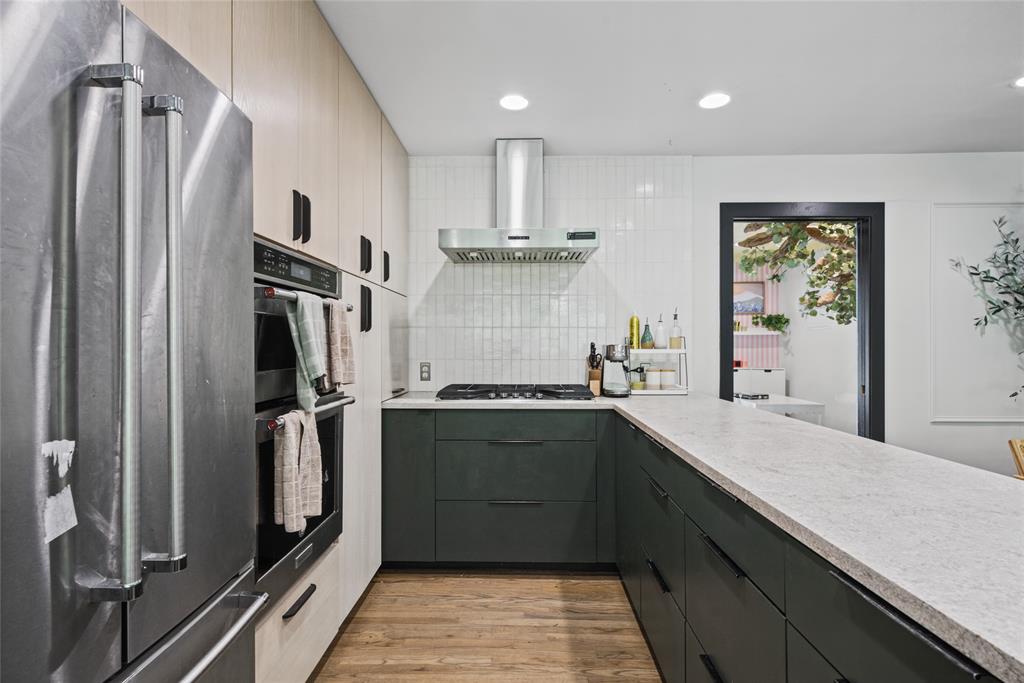 Kitchen featuring two-tone cabinetry, stainless steel double wall oven, gas cooktop with stainless steel range hood, stone-finish countertops, and wood-finish flooring