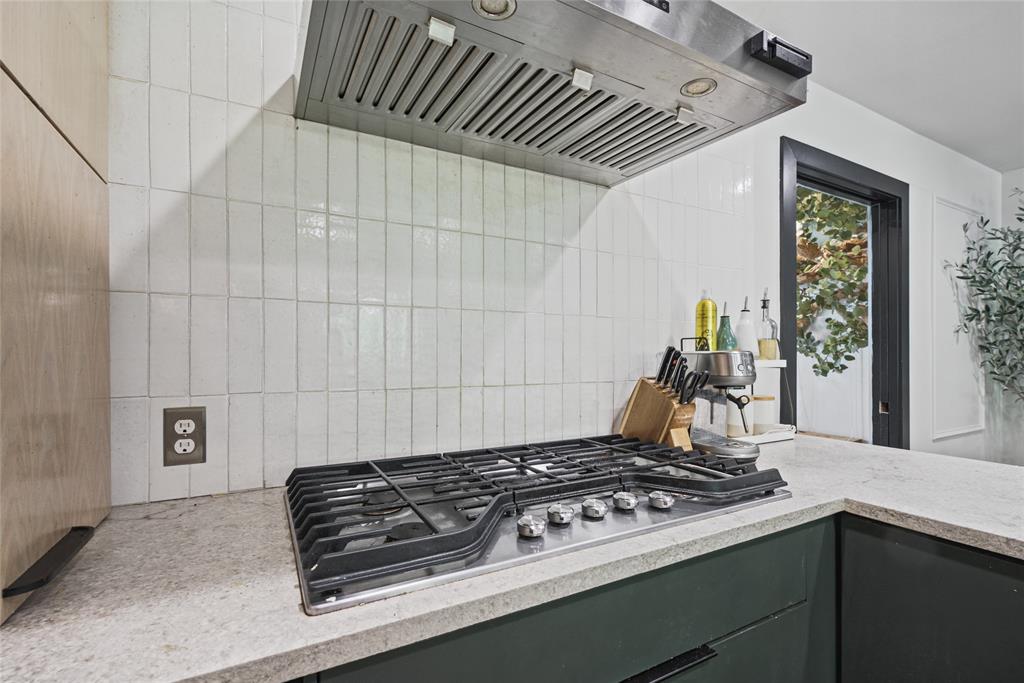 Stainless steel gas cooktop with a professional-grade range hood, vertical white subway tile backsplash, solid-surface countertops, and dark-toned cabinetry