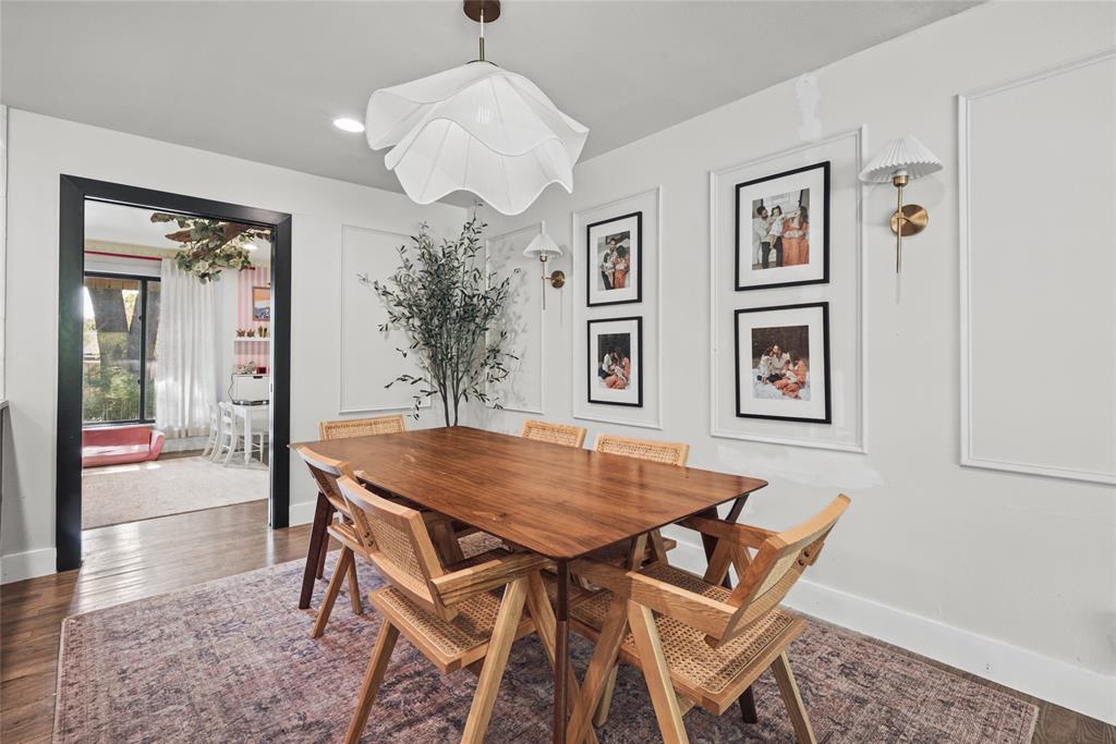 Dining area featuring detailed wall molding, wood-finish flooring, a contemporary floral-shaped pendant light, and two brass-finish wall sconces