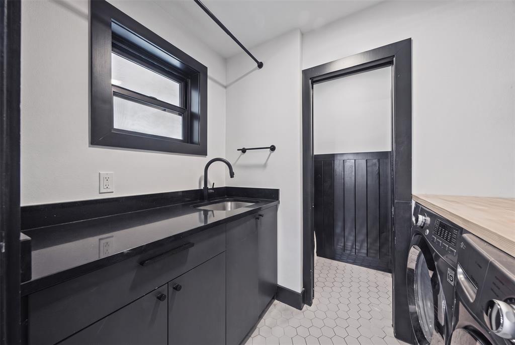 Laundry space featuring matte black cabinetry, dark stone-finish countertops, stainless steel undermount sink with a matte black faucet, hexagonal floor tiling, and black-trimmed woodwork