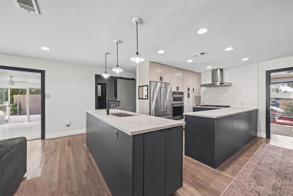 Kitchen featuring dual-tone cabinetry, stone-finish countertops, stainless steel appliances, pendant lighting, and wood-finish flooring