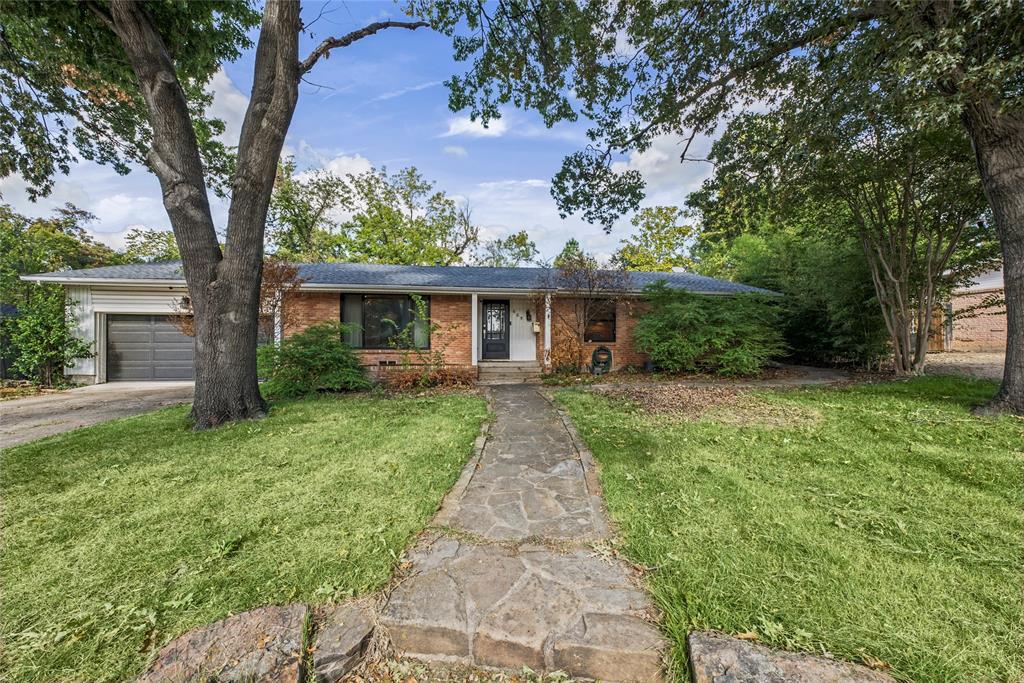 Single-story brick exterior featuring a stone walkway, attached garage, and mature trees