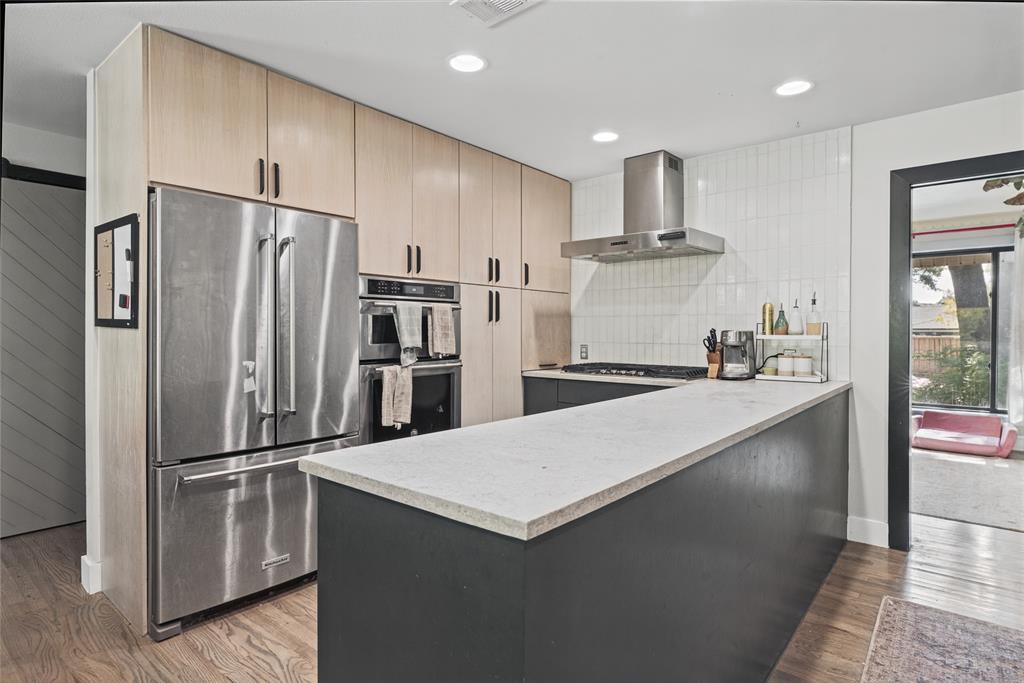 Kitchen featuring light-finish cabinetry, stainless steel appliances, a solid-surface breakfast bar, subway-tiled backsplash, and wood-finish flooring