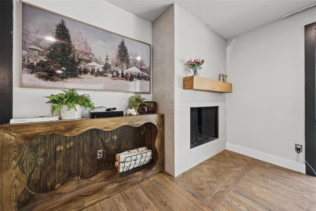 Fireplace featuring a textured tiled surround and a natural wood mantel, complemented by herringbone-patterned wood-finish flooring