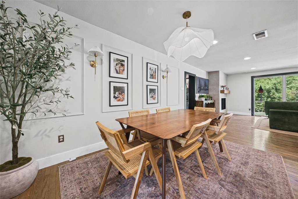 Dining area featuring wall molding panels, decorative brass wall sconces, a contemporary pendant light, wood-finish flooring, and a fireplace with a textured surround