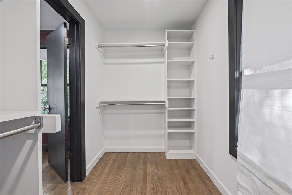 Walk-in closet featuring white built-in shelving, dual-tier metal hanging rods, and wood-finish flooring