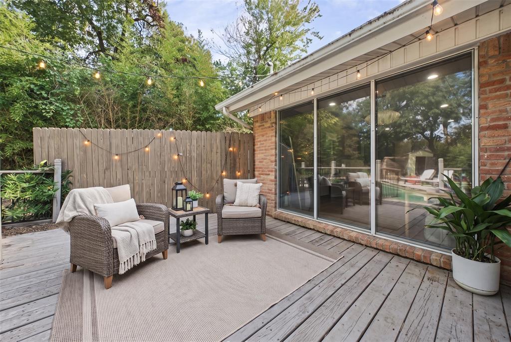Wood-plank decking, floor-to-ceiling glass sliding doors, brick exterior siding, and perimeter privacy fencing