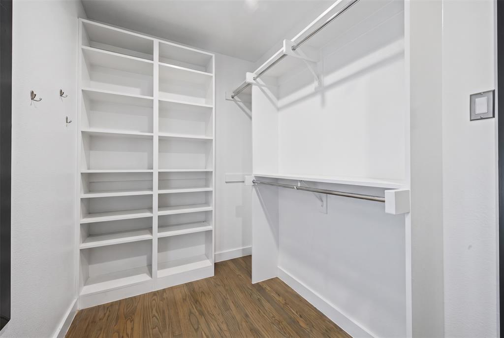 Walk-in closet featuring floor-to-ceiling built-in shelving, dual-level hanging rods, wall-mounted hardware hooks, and wood-finish flooring