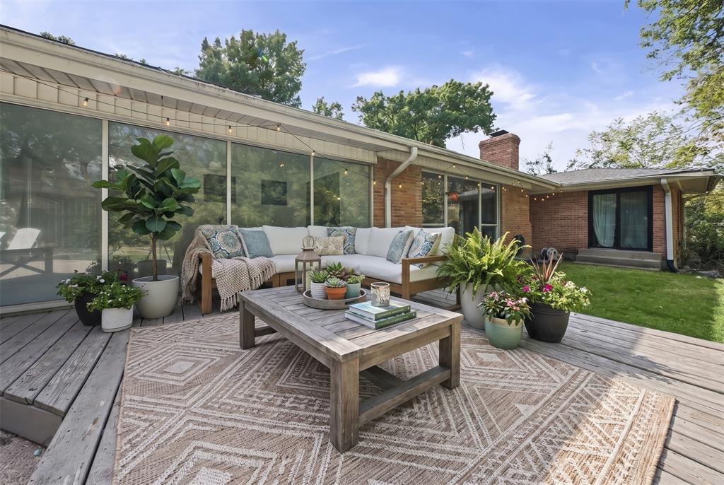 Spacious wood deck featuring floor-to-ceiling glass paneling, exposed brick exterior cladding, a brick chimney, and a landscaped lawn area