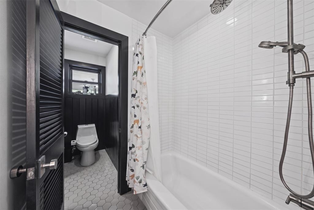 Bathroom featuring white vertical tile shower surround, chrome multi-function shower fixture, hexagonal floor tile, and black louvered door