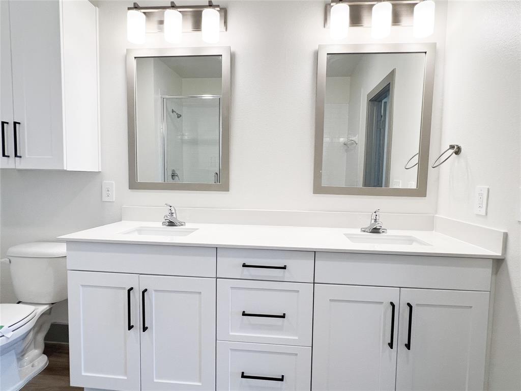 Bathroom with double vanity, a shower stall, and dark wood-style floors
