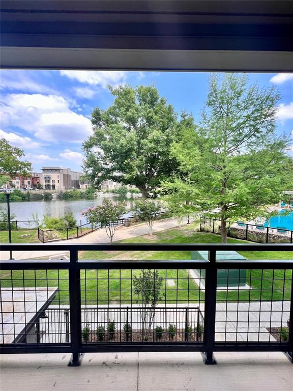 Balcony with black metal grid railing, concrete flooring, and surrounding trees