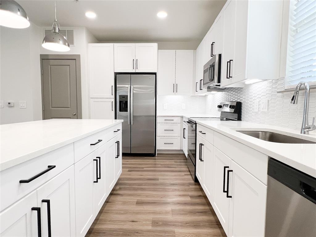 Kitchen featuring stainless steel appliances, white cabinetry, backsplash, light stone countertops, and light wood finished floors