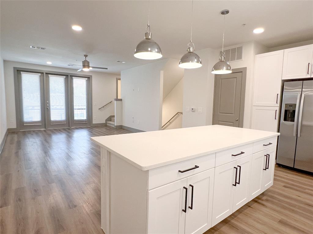 Kitchen with stainless steel fridge, hanging light fixtures, white cabinets, recessed lighting, and a center island
