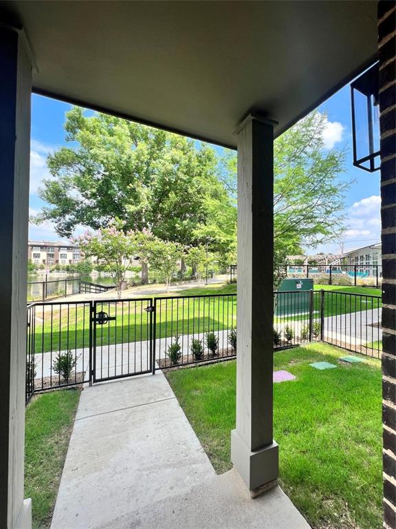 Covered porch featuring a concrete patio, brick exterior wall, and metal light fixture, opening to a fenced yard with a concrete walkway and manicured lawn