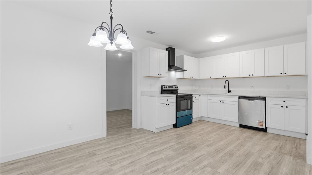 Kitchen featuring white shaker-style cabinetry, wood-finish flooring, a stainless steel dishwasher, a black range hood, and a five-light chandelier