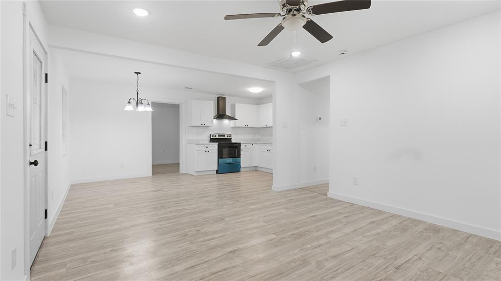 Open floor plan featuring wood-finish flooring, white shaker cabinetry, stainless steel range with overhead hood, multi-arm chandelier, and ceiling fan with lighting