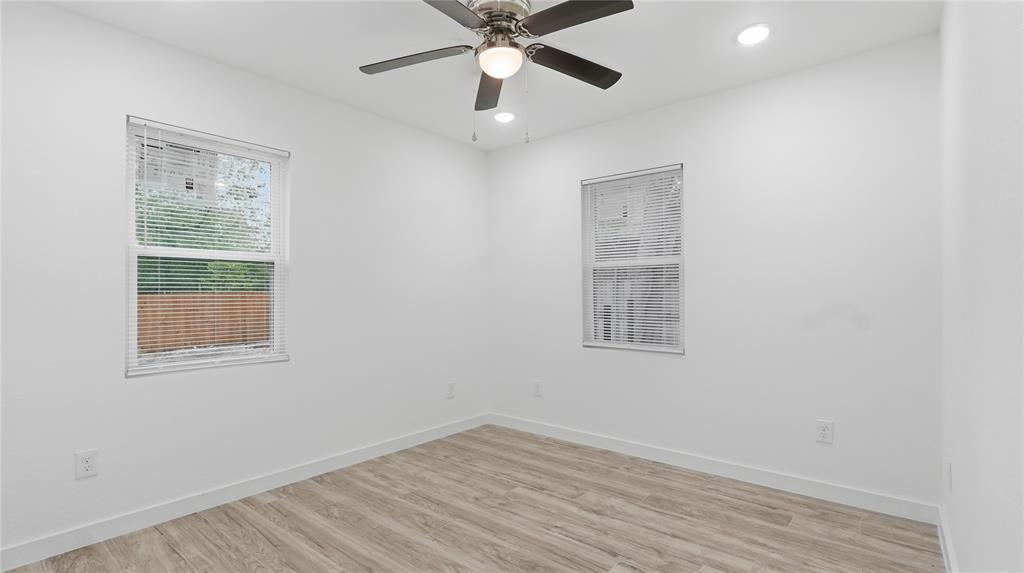 Neutral-toned interior space featuring wood-finish flooring, two dual-pane windows, recessed ceiling lighting, and a multi-blade ceiling fan with an integrated light fixture