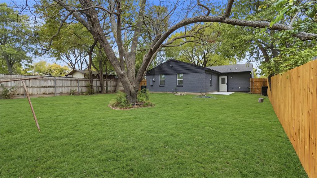 Expansive backyard featuring a manicured lawn, mature trees, wood privacy fencing, and a concrete patio