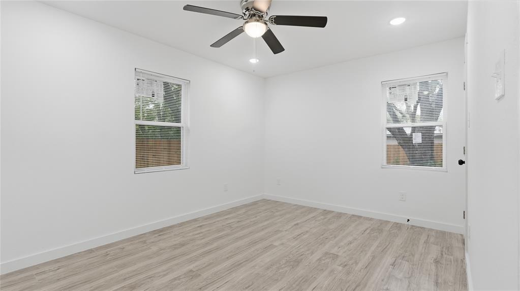 Neutral interior featuring wood-finish flooring, two dual-pane windows, and a ceiling fan with integrated lighting