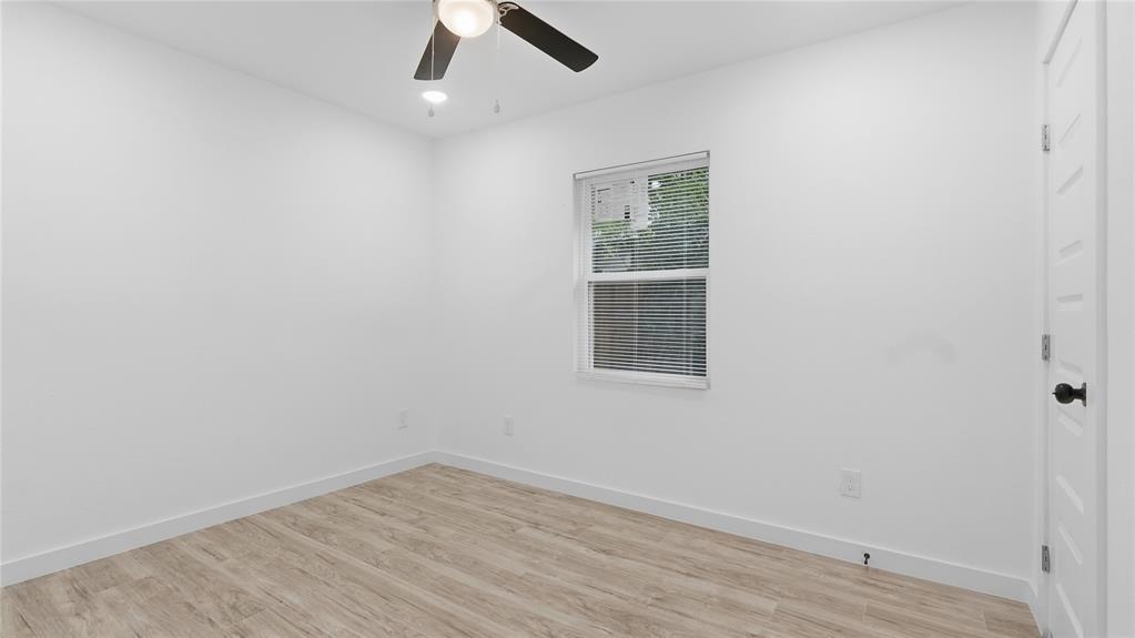Neutral-toned wood-finish flooring, white walls, single-hung window, and ceiling fan with integrated lighting
