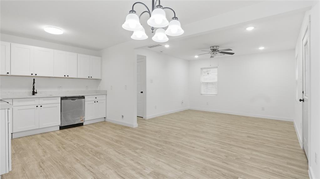 Kitchen featuring white shaker cabinetry, stone-finish countertops, stainless steel dishwasher, five-light chandelier, and wood-finish flooring