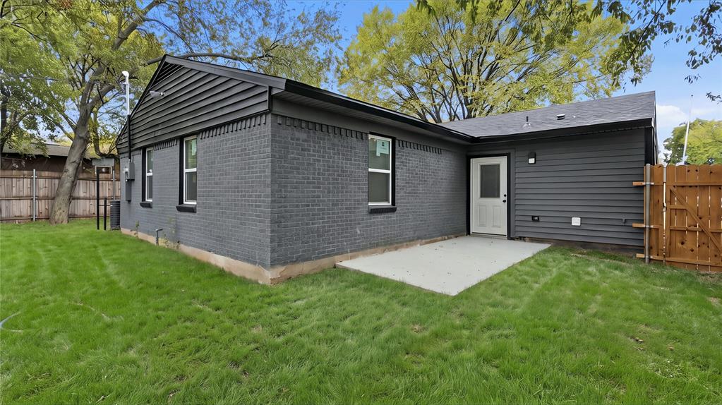 Exterior featuring dark-toned brick and horizontal siding, a concrete patio, a rear entry door with glass insert, and wood fencing