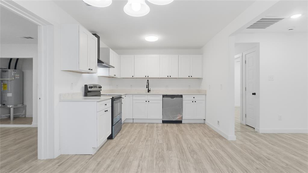 Kitchen featuring white shaker-style cabinetry, light-toned stone countertops, wood-finish flooring, stainless steel appliances, and a matte black pull-down faucet