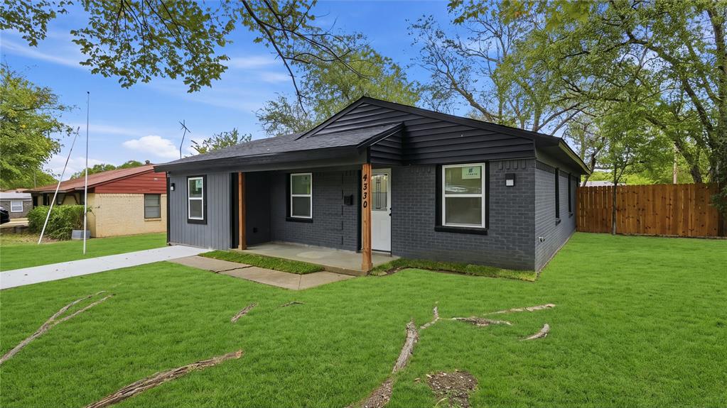 Exterior facade featuring dark grey brick, horizontal wood siding, a covered front porch with natural wood support posts, and white window frames