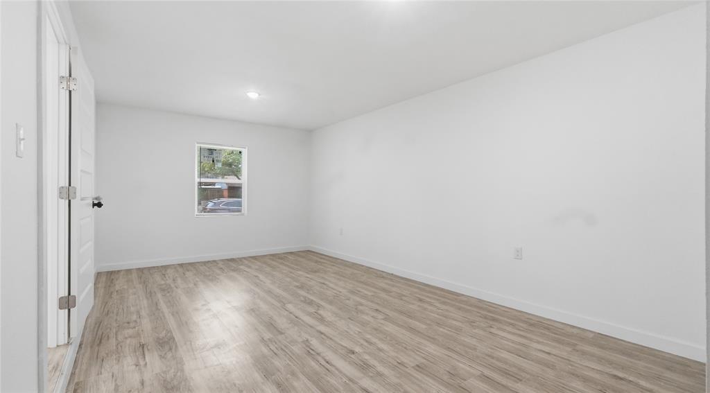 Room interior featuring wood-finish flooring, white walls, recessed ceiling lighting, and a single-pane window