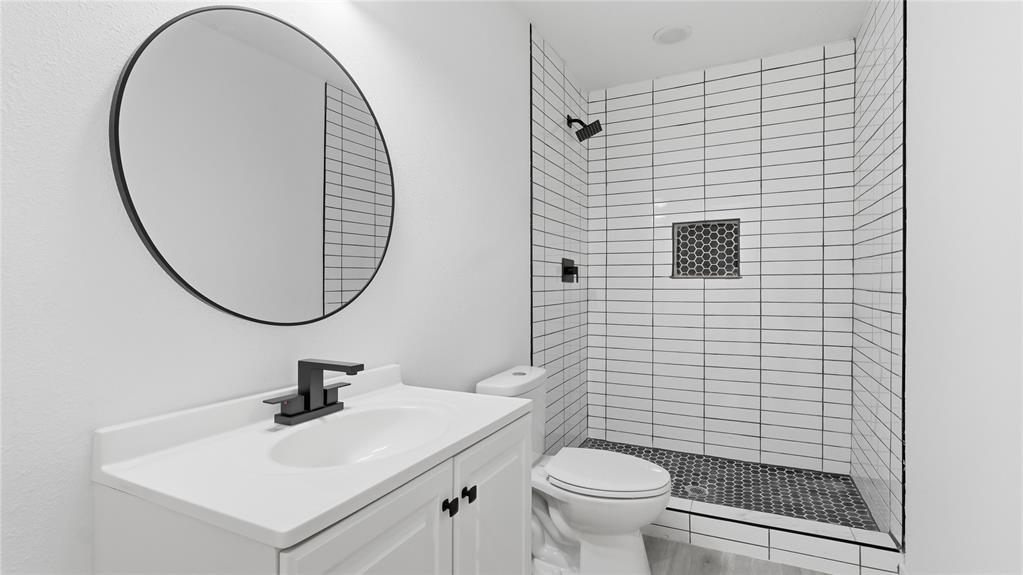 Bathroom featuring a white vanity with a neutral countertop, round mirror, matte black plumbing fixtures, walk-in shower with white wall tile, and patterned floor tile