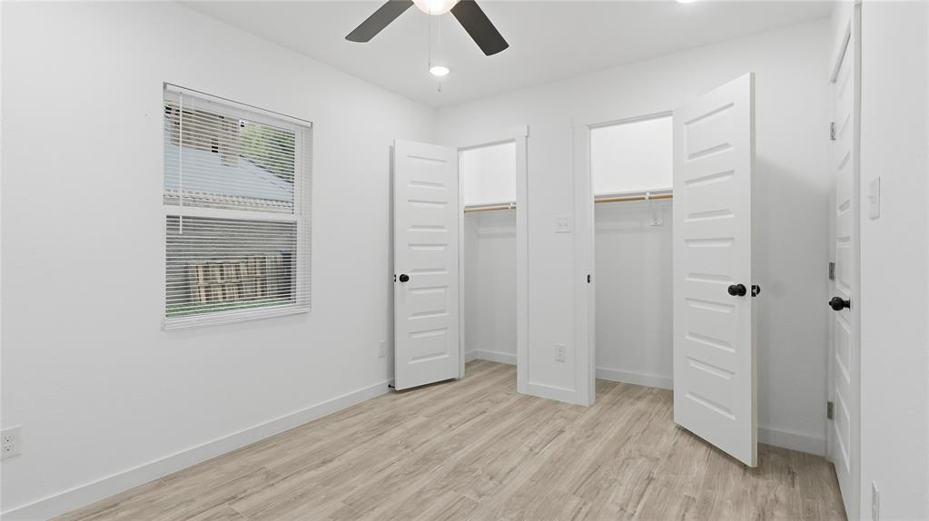 Wood-finish flooring, dual-door closets, paneled doors with matte black hardware, and ceiling fan with integrated lighting