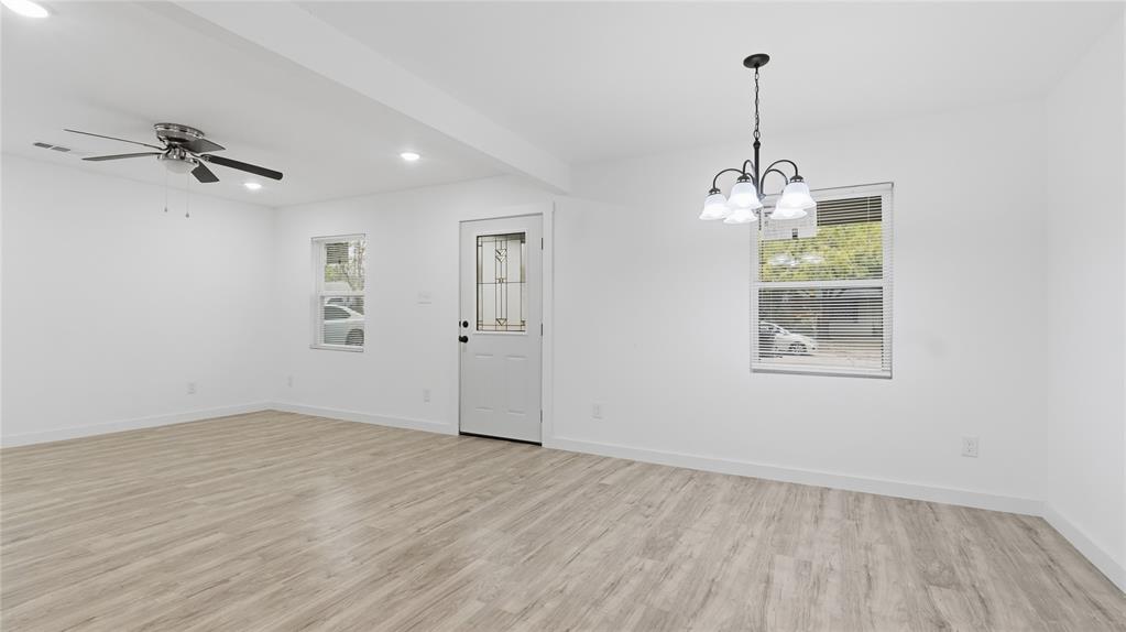 Open-concept interior featuring wood-finish flooring, a five-light chandelier, a ceiling fan with integrated lighting, and an exterior door with leaded glass inlay