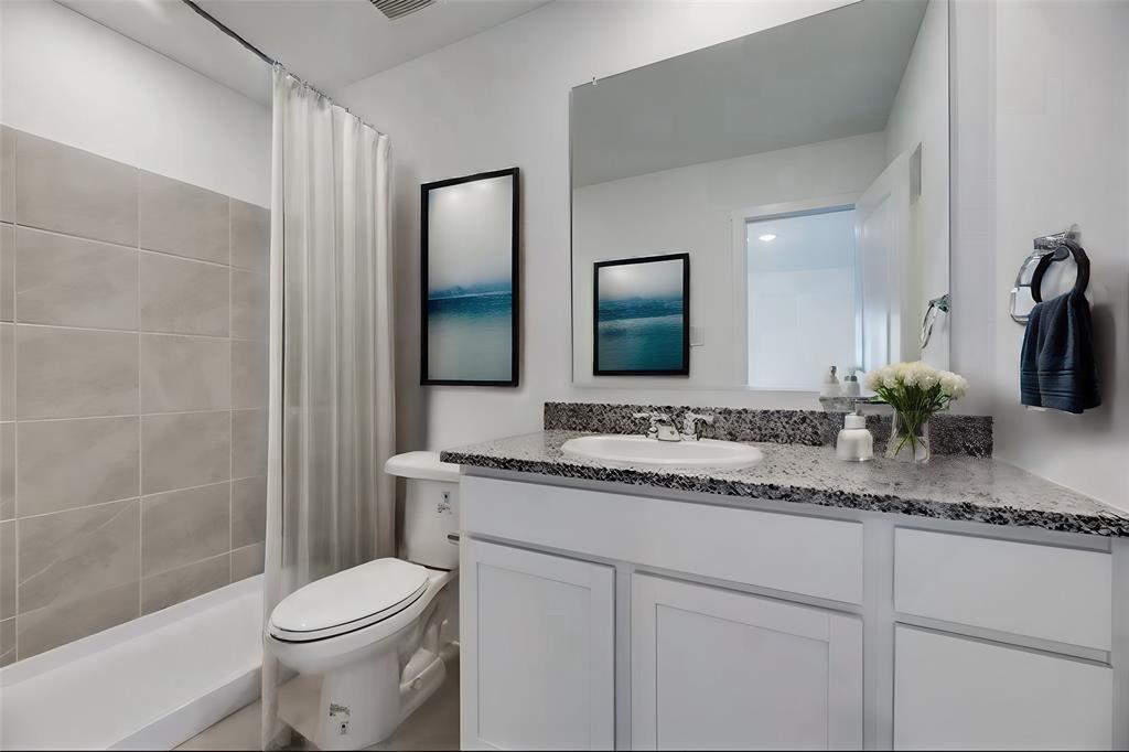 Bathroom featuring a vanity with shaker-style white cabinetry, stone-finish countertop, integrated basin, and a large wall-mounted mirror