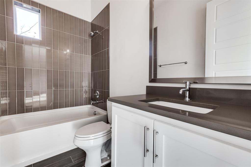 Bathroom featuring a white vanity cabinet with a dark countertop, integrated sink, vertical tile surround in the shower area, and a large wall-mounted mirror