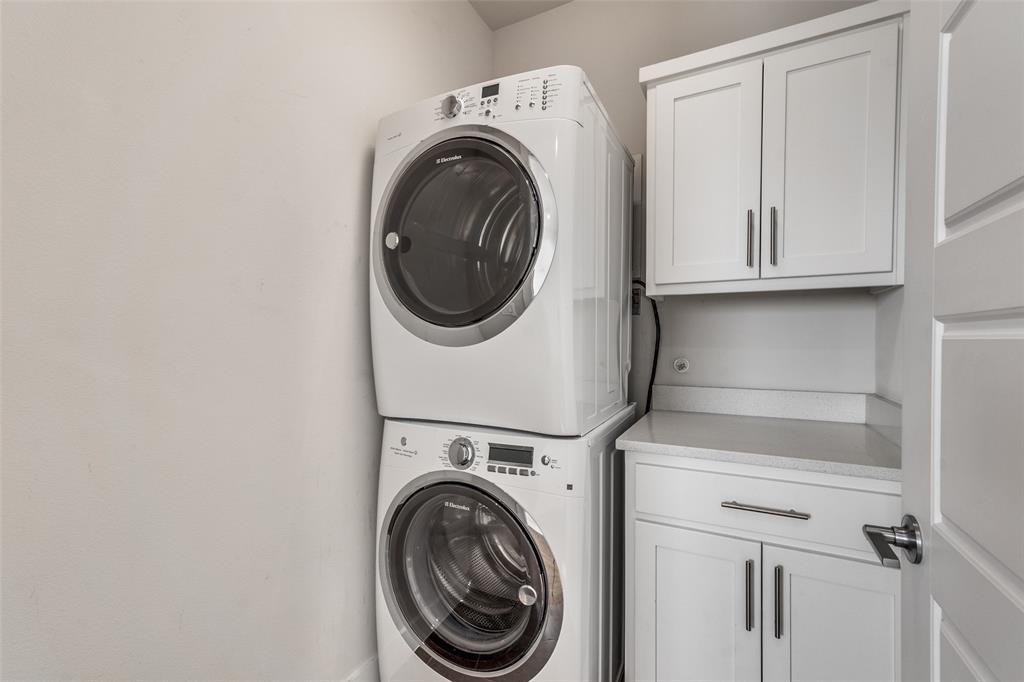 Laundry area featuring a stackable washer and dryer, white shaker-style cabinetry, and solid surface countertop