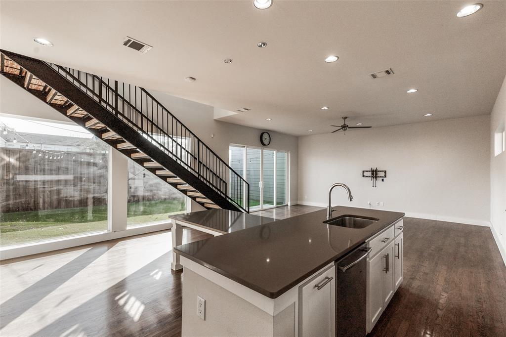 Open-concept space featuring an industrial-style staircase with metal railings, a central island with a stone-surfaced countertop, stainless steel under-mount sink, recessed lighting, and wood-finish flooring