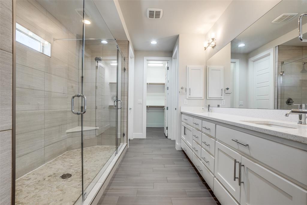 Bathroom featuring a glass-enclosed shower with tiled walls and a stone-style shower floor, double vanity with white cabinetry, quartz countertop, and large-format tile flooring