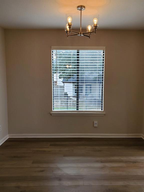 Room featuring wood-finish flooring, a multi-arm chandelier with glass shades, and a window with horizontal blinds