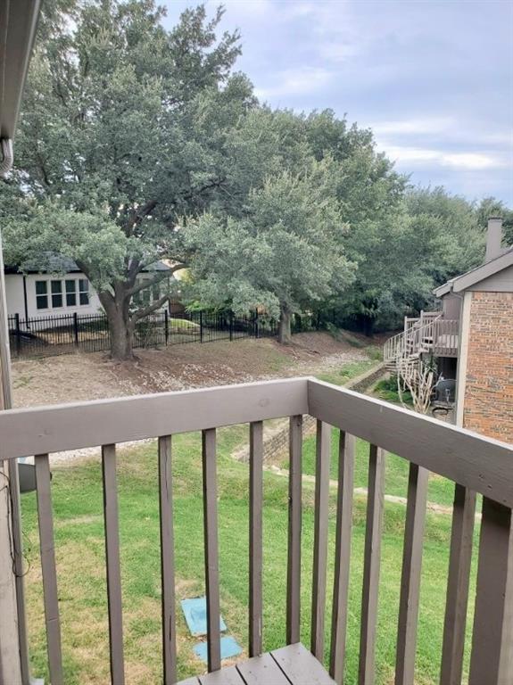 Elevated balcony with wooden railing overlooking a sloped lawn, stone retaining wall, and mature trees