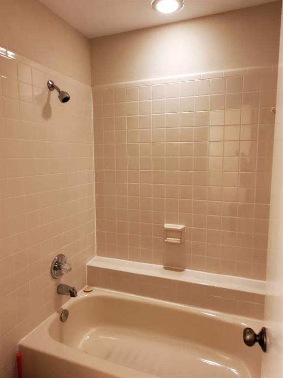 Bathtub with an integrated shower, chrome fixtures, built-in soap dish, and ceramic tile surround