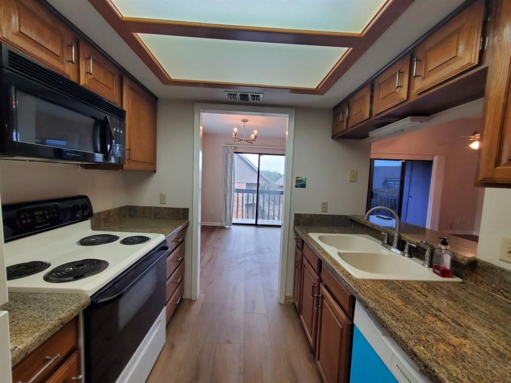 Kitchen featuring wood cabinetry, stone-finish countertops, dual-basin sink, built-in microwave, and recessed tray lighting