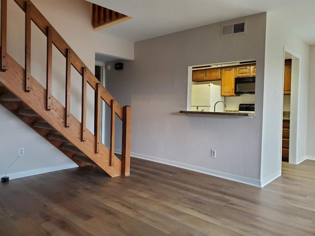 Wood-finish flooring throughout, wooden staircase with open-rail design, and kitchen pass-through window with a solid surface ledge