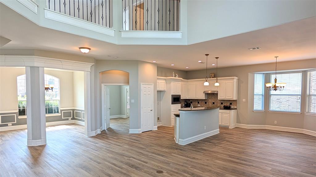 Open-concept interior featuring wood-finish flooring, a two-story ceiling with a decorative mezzanine railing, white cabinetry, a peninsula island, and arched architectural detailing