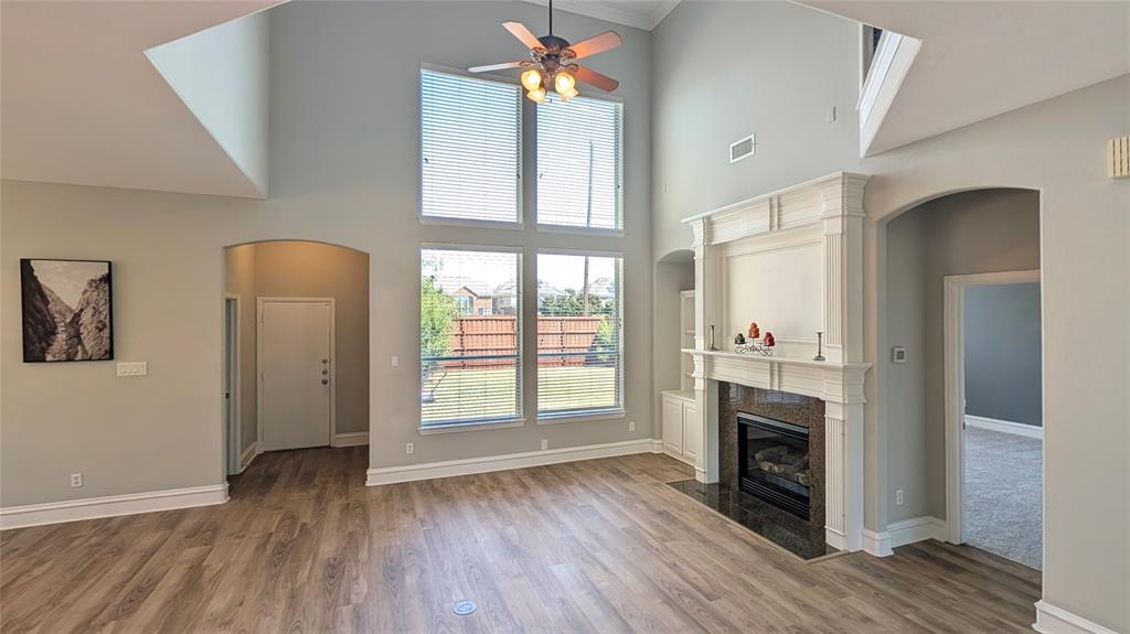 Vaulted ceilings featuring a central fan, fireplace with a decorative mantel, wood-finish flooring, and expansive windows