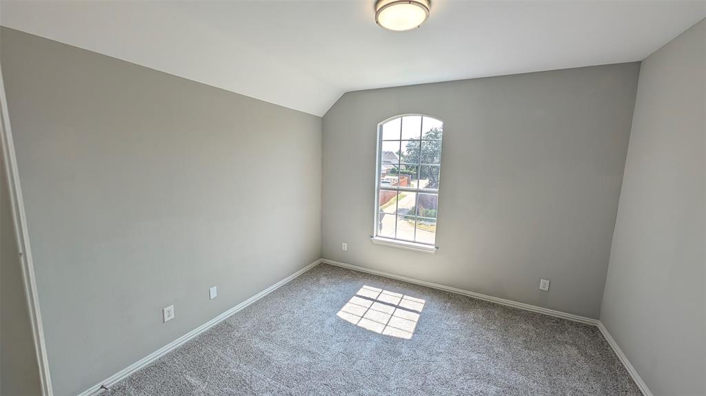 Neutral-toned interior space featuring carpeting, an arched multi-pane window, and a flush-mount light fixture