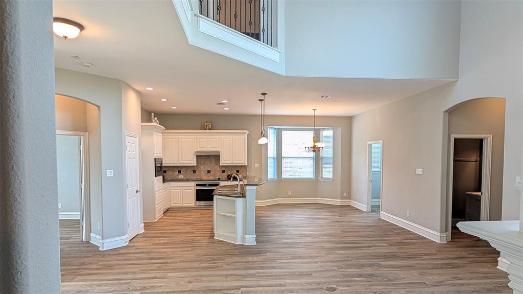 Open-concept kitchen featuring white cabinetry, wood-finish flooring, a center island with sink, and double-height ceilings with an overlook
