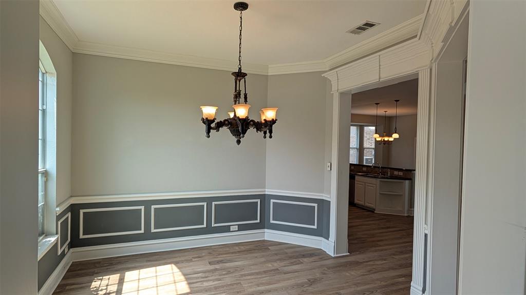 Interior space featuring wood-finish flooring, two-toned walls with wainscoting, crown molding, arched window, and a multi-light chandelier