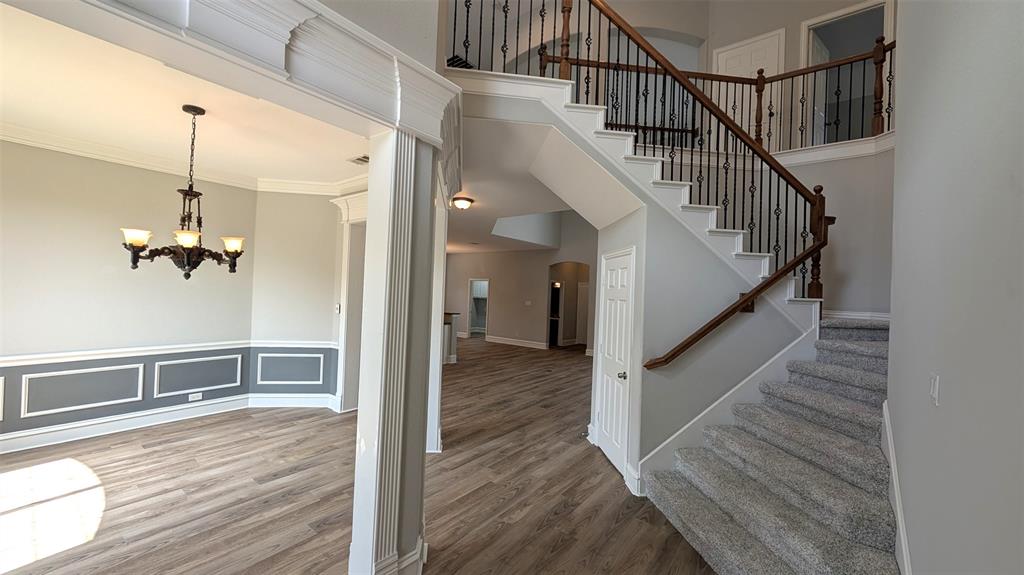 Foyer featuring wood-finish flooring, a staircase with decorative metal balusters and wooden handrail, wainscoting, and a multi-arm chandelier