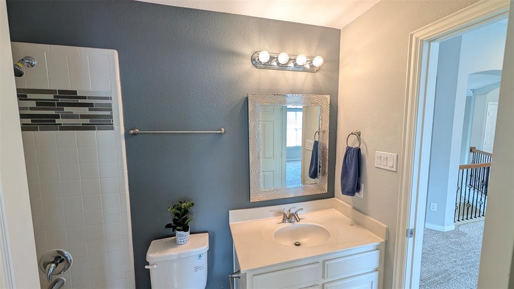 Bathroom featuring a white vanity with a composite countertop, an integrated sink, a framed wall mirror, four-bulb vanity lighting, and a shower with tile surround and decorative horizontal accent inlay